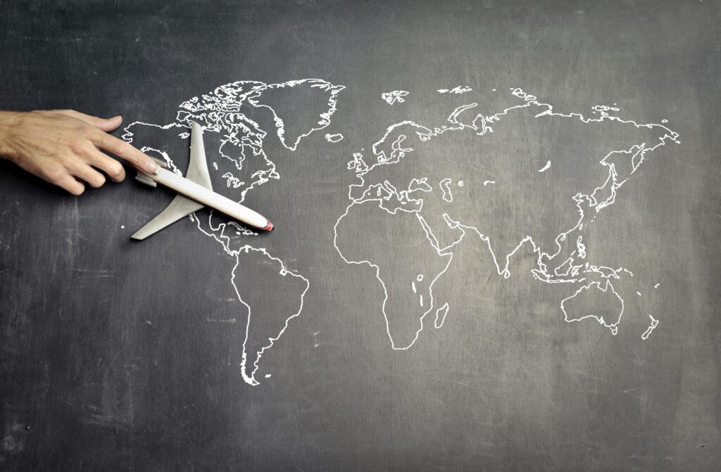 From above of crop anonymous person driving toy airplane on empty world map drawn on blackboard representing travel concept