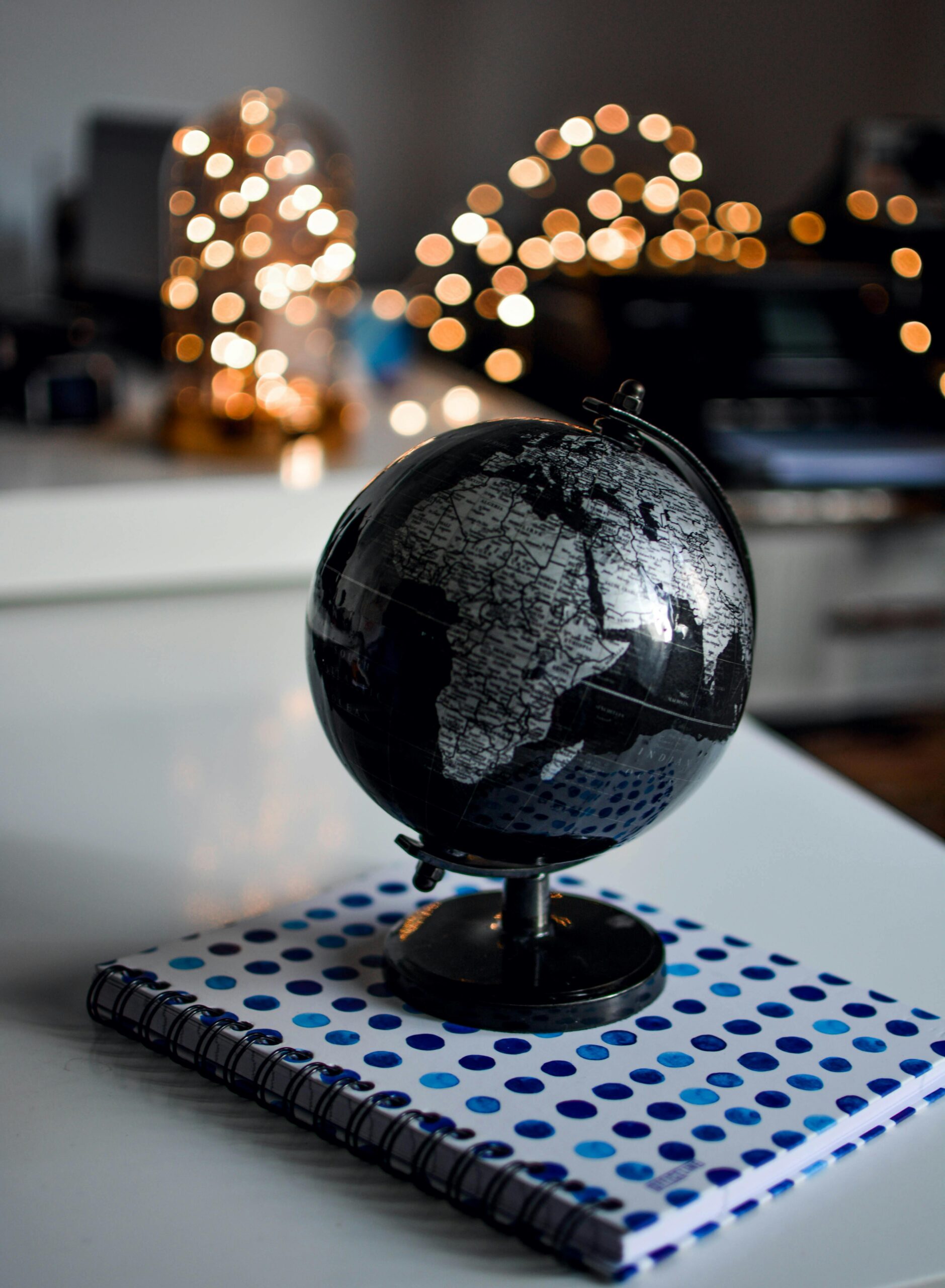 Elegant black globe and notebook against warm bokeh lights, perfect for educational themes.